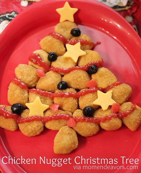 Christmas tree shaped arrangement of golden brown chicken nuggets, drizzled with ketchup and decorated with small cheese stars and blueberries, served on a red platter.